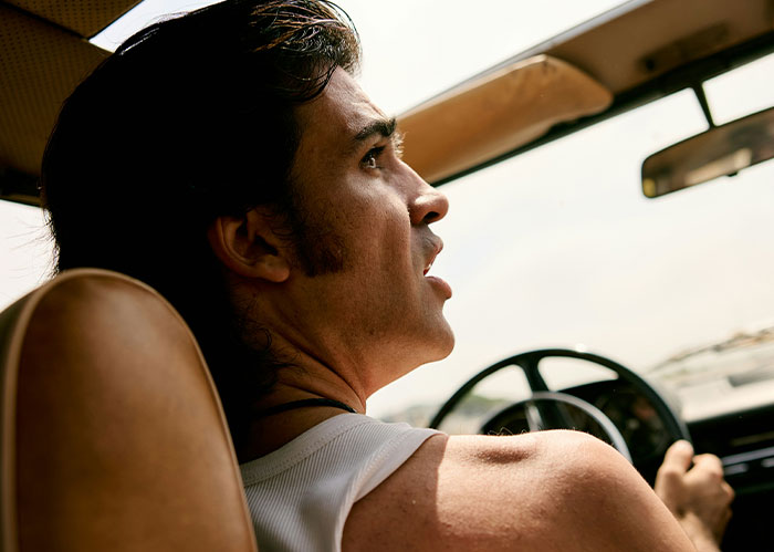 Man driving a car inside, looking back with concern, depicting a scene related to police chasing the wrong person.