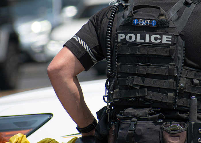Police officer wearing tactical vest with police patch, standing near white car during a chase of the wrong person.