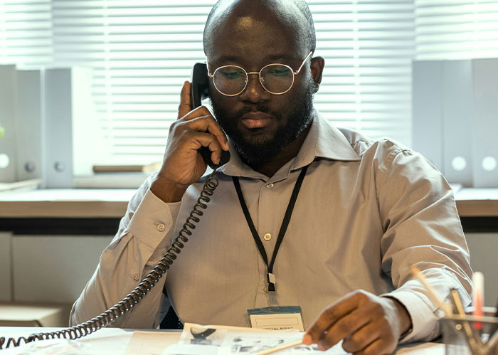 Man with glasses on phone researching funny scary wild stories about police chasing wrong person in office.