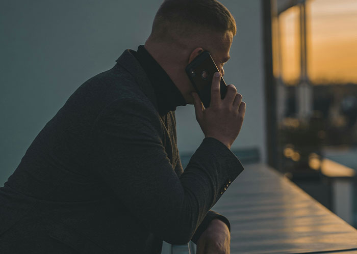 Man in dark jacket talking on phone outdoors during sunset, illustrating police chasing the wrong person stories.
