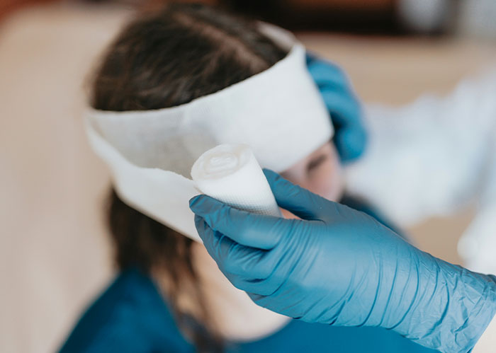 Person wearing a white bandage on head with a hand in blue gloves holding gauze, related to police chasing the wrong person.