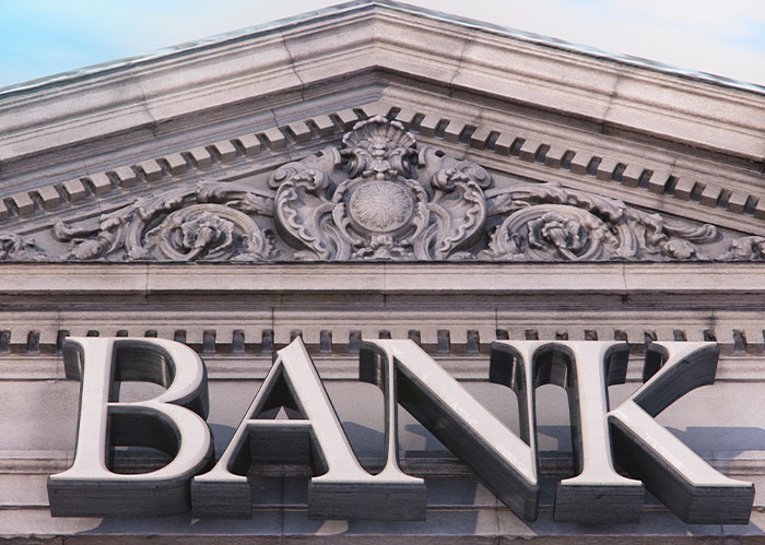 Close-up of ornate bank building facade with detailed stone carvings above large bold BANK letters.