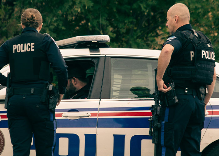 Two police officers in tactical gear standing next to a police car during a wild police chase incident.