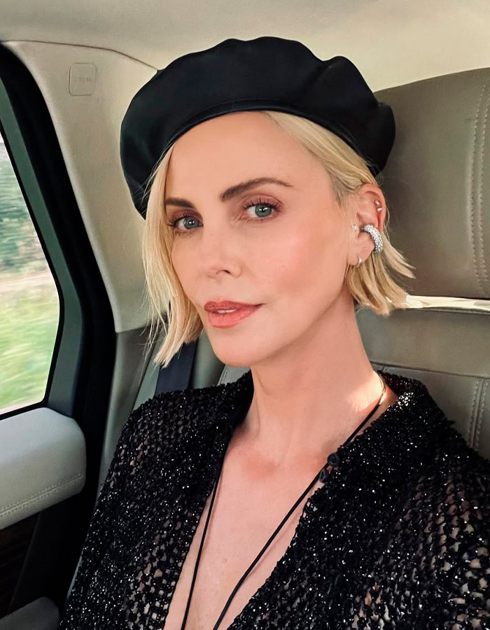 Charlize Theron wearing a black beret and sparkly top inside a car, linked to internet divided over ballet comment.