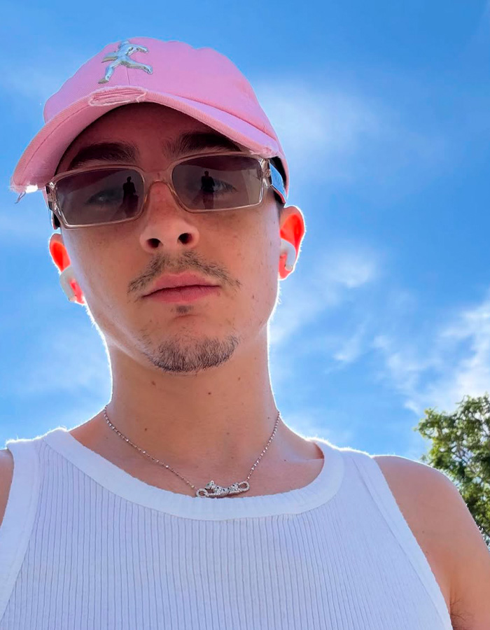 Young man wearing pink cap and sunglasses outdoors with clear blue sky, related to Timothee Chalamet ballet comment debate.