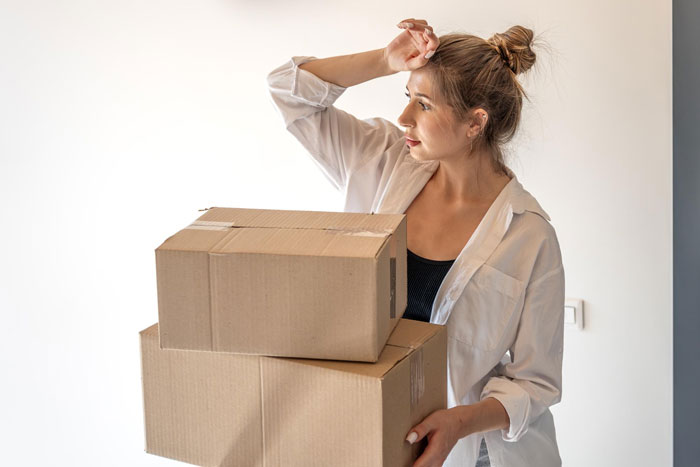 Young woman holding moving boxes, appearing thoughtful and determined, illustrating boyfriend plans to leave girlfriend theme.