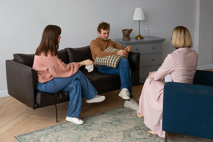 Couple in therapy session, man looking remorseful while woman holds tissues, addressing relationship and cheating issues.