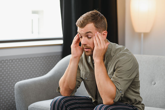 Man sitting on a couch holding his head in frustration, reflecting on destroying life chasing a fantasy.