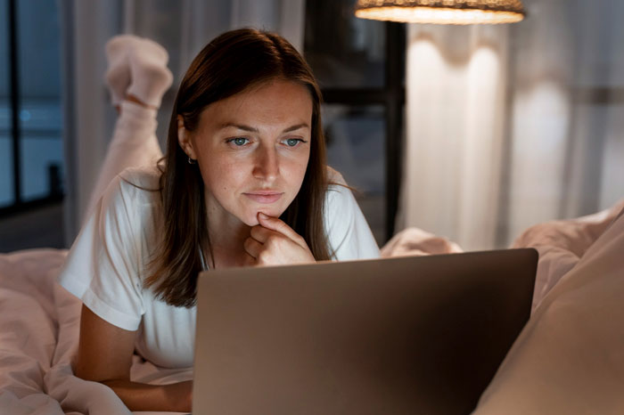 Woman researching criminal and cheater cases on laptop late at night in cozy bedroom with warm lighting
