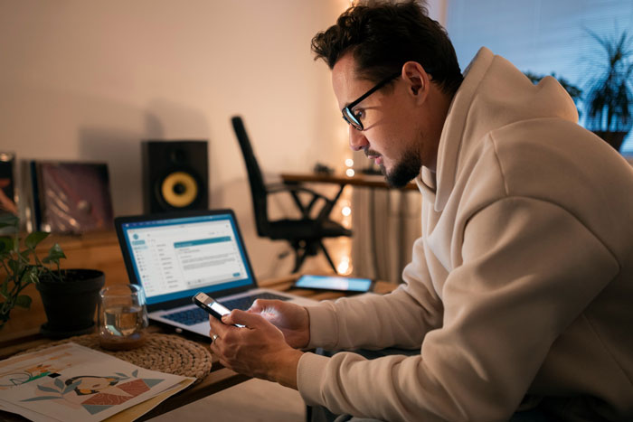 Man in glasses using smartphone and laptop, unaware of secret recording on husband's PC sessions. Man in glasses using smartphone and laptop, unaware of secret recording on husband's PC sessions.