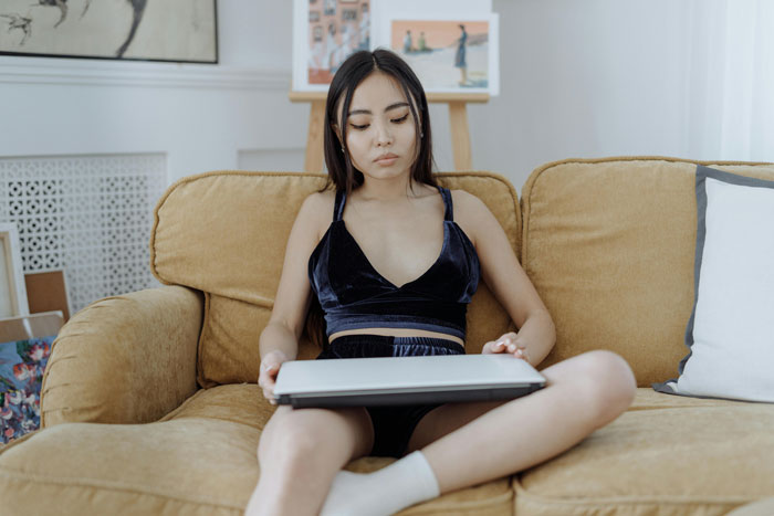 Woman sitting on couch holding a laptop, representing wife getting cheeky with lover on husband's PC scenario. Woman sitting on couch holding a laptop, representing wife getting cheeky with lover on husband's PC scenario.