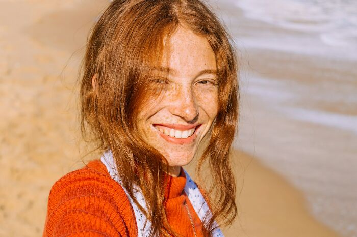 Young woman smiling on the beach reflecting on normal family activities that now seem bizarre in hindsight.
