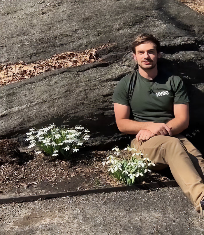 Young New York Botanical Garden scientist sitting by flowers outdoors wearing NYBG shirt in natural setting Young New York Botanical Garden scientist sitting by flowers outdoors wearing NYBG shirt in natural setting