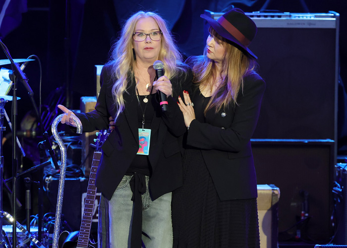 Two women on stage, one holding a microphone, reflecting on Christina Applegate&rsquo;s hospitalization and loved ones&rsquo; fear.
