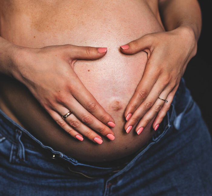 Pregnant woman with painted nails forming a heart on her belly, representing baby peeing inside the womb concept.