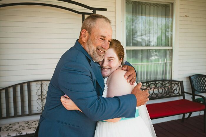 A bearded dad in a blue suit hugs his daughter, who wears a wedding dress with a blue sash. Raising daughters.