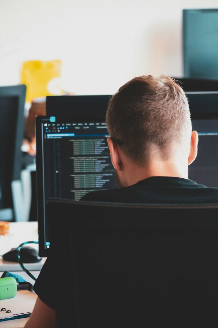 Man from behind, coding on a computer, perhaps considering to rage quit their jobs due to stress or frustration.