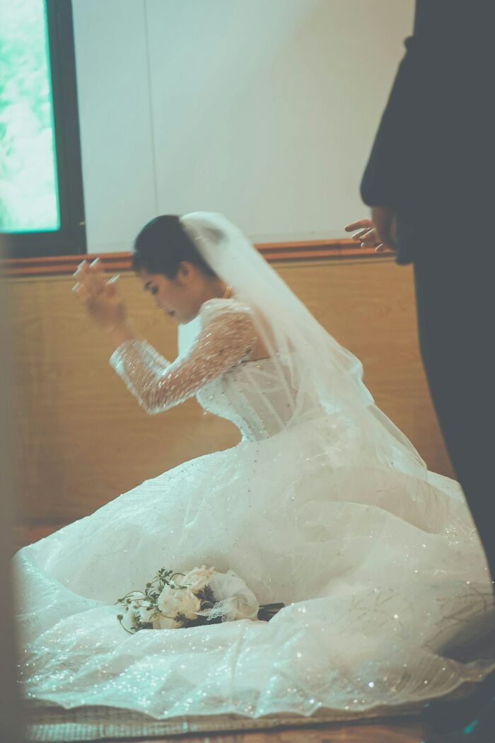 Bride in a sparkling wedding dress kneeling with bouquet on the floor, depicting trashy tacky and distasteful wedding stories.