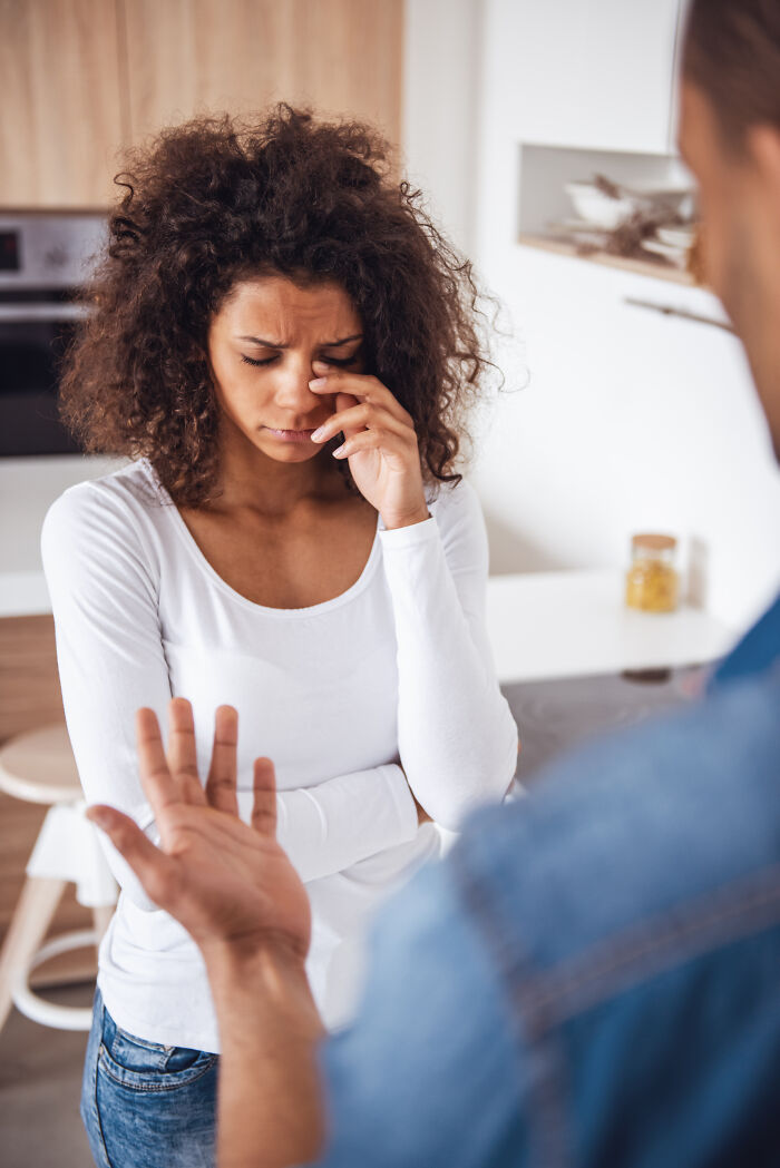 A distraught woman with curly hair, wiping her eyes, while a man's outstretched hand is in the foreground, highlighting being cheated on.