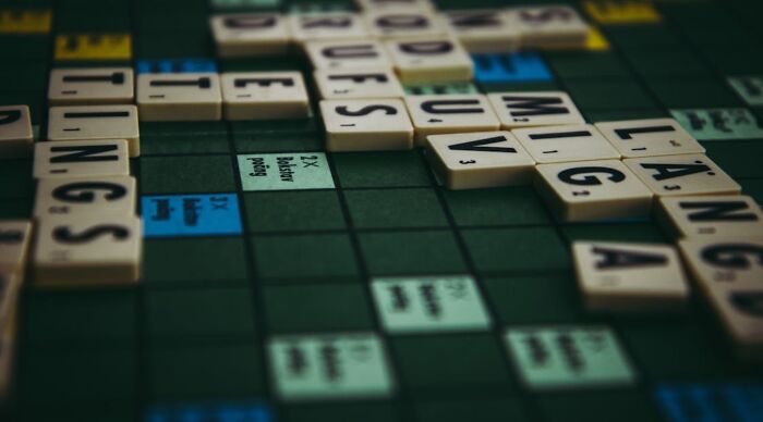 A close-up of a Scrabble board with words like "TINGS" and "L&Aring;NG" formed by letter tiles, illustrating visual word clues.