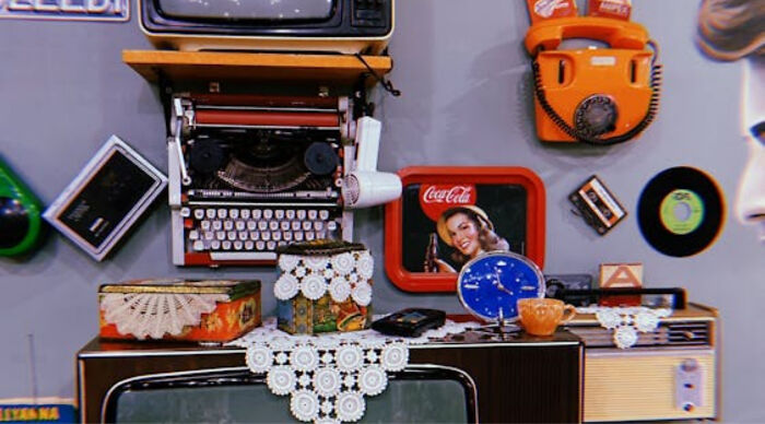 Vintage 1960s pop culture items including a typewriter, rotary phone, records, and retro Coca-Cola decor displayed on a shelf.