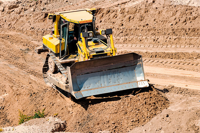 A large yellow bulldozer moving dirt at a construction site. This image evokes family crimes and unhinged stories.