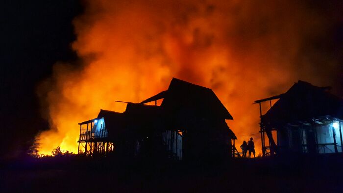 Silhouetted homes and people stand against a fiery orange blaze, evoking unhinged crimes.