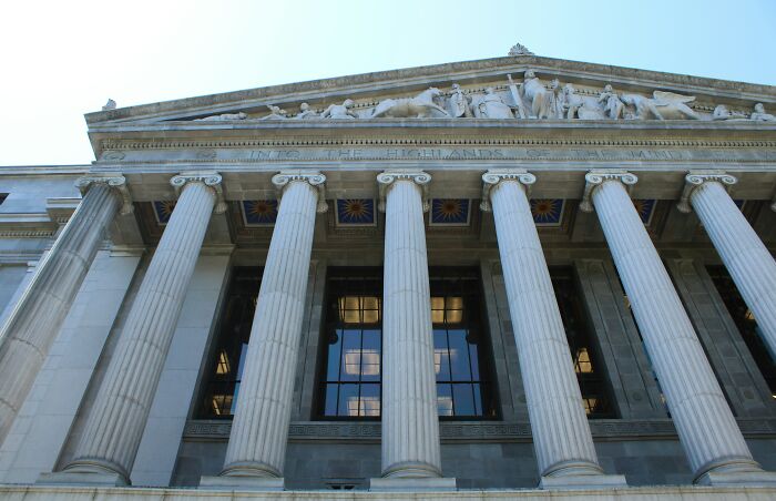 A grand stone building with large columns and classical sculptures. Symbolizes justice and family crimes.