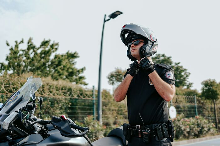 A police officer in black uniform and sunglasses adjusts his helmet next to his motorcycle, ready to fight crimes.