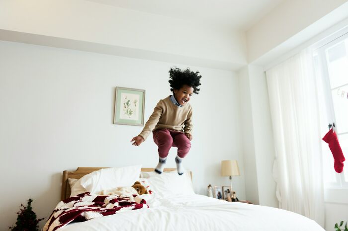 Child jumping on bed indoors, illustrating kids with no survival instincts through playful and risky childhood behavior.