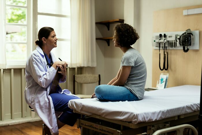 Doctor in white coat talking to patient sitting cross-legged on exam table, illustrating karma stories satisfying outcomes.