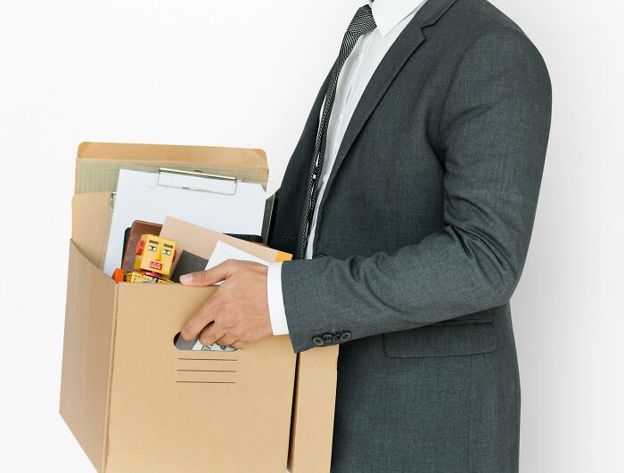 Man in a suit holding a box of personal items, symbolizing employees quitting their job immediately and leaving work for good.