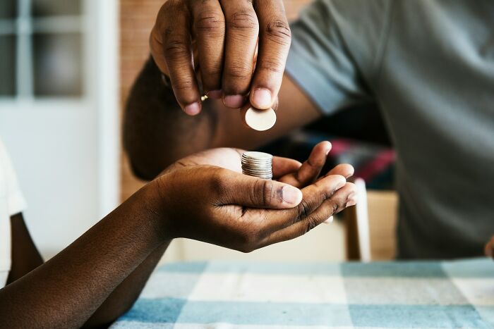 A man placing coins in a child's hand, demonstrating financial lessons for dads raising daughters.