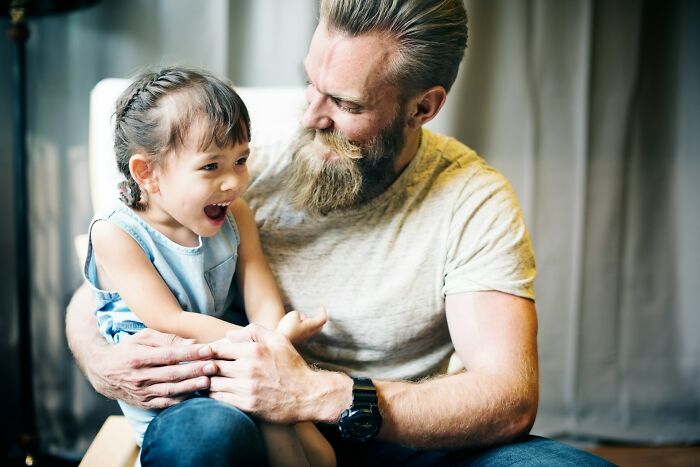A bearded dad holding his laughing daughter, receiving advice for raising daughters.
