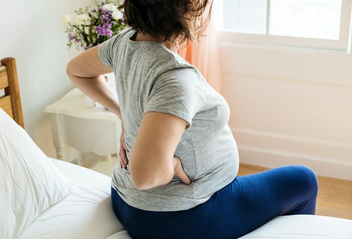 Pregnant woman sitting on bed holding lower back in discomfort, illustrating challenging gynecologist appointments.