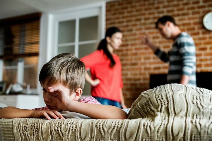 Child covering face on couch while parents argue in background, illustrating bizarre family moments people once found normal