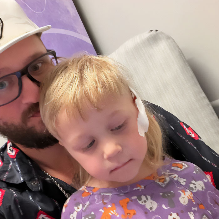 Man wearing glasses comforting young child with bandage on head after Walmart police attack incident.