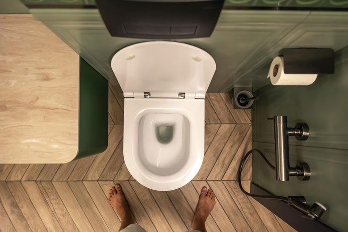 Bare feet on a wooden floor, standing before a wet toilet seat. A scene highlighting a gross dad.