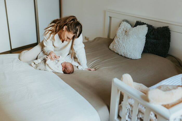 Young mother caring for her newborn on the bed, illustrating emotional moments linked to weaponized incompetence stories.