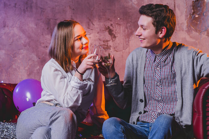 Young couple on a mid-date toast, sharing drinks and smiles in a cozy setting, capturing unhinged dating moments.