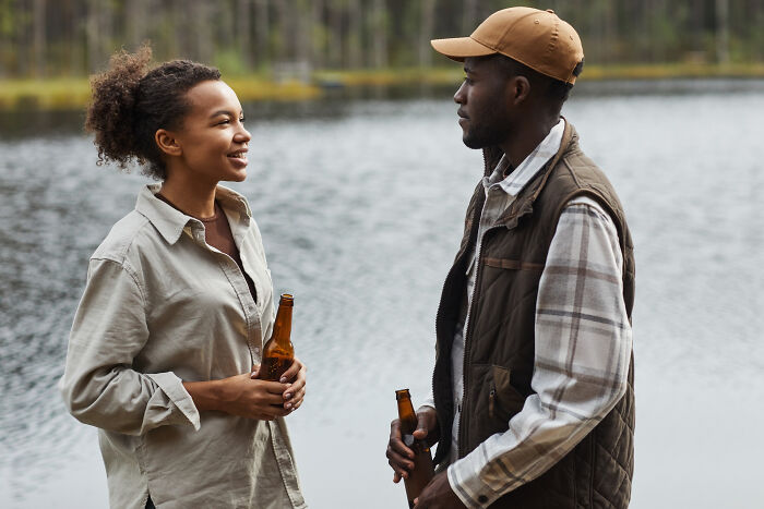 A young couple enjoying drinks by the lake during a casual outdoor date conversation on a cool day.