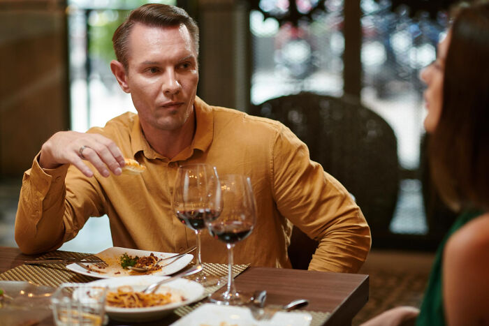 Man in a mustard shirt eating dinner with wine, showing unhinged reasons people left mid-date at a restaurant.