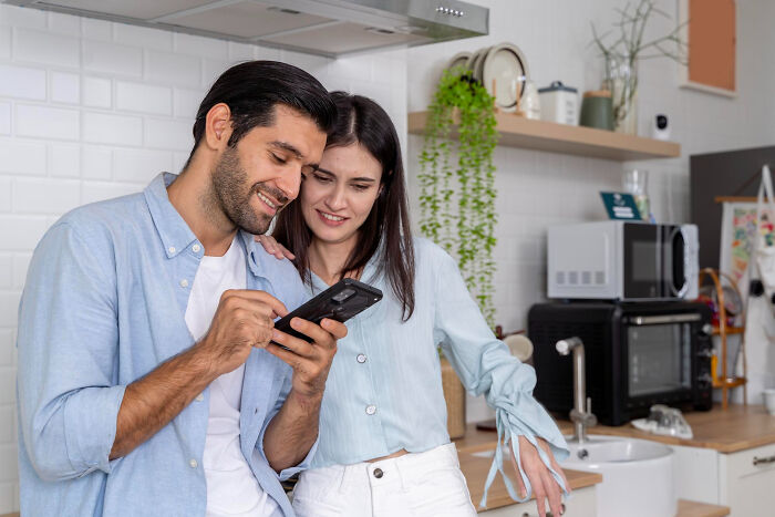 A happy couple in a kitchen looking at a phone together, illustrating reasons people left mid-date scenarios.