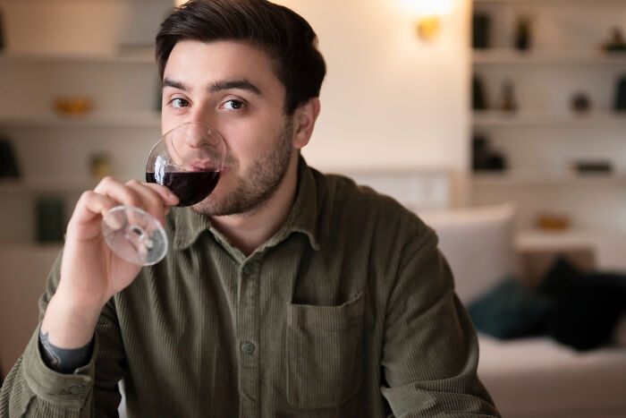 Man in casual shirt sipping red wine at home, illustrating unhinged reasons people got up and left mid-date.