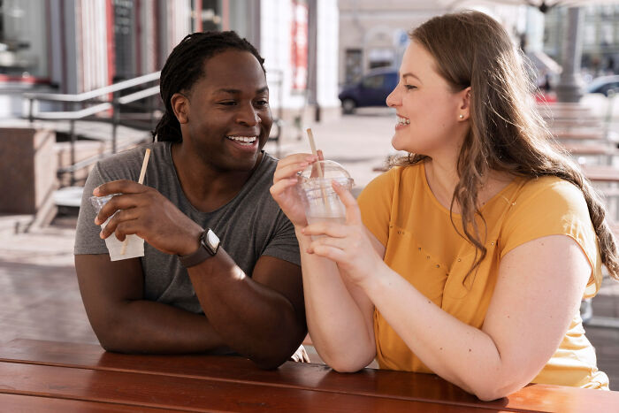A couple smiling and chatting over drinks outdoors, capturing a lighthearted moment during a mid-date encounter.