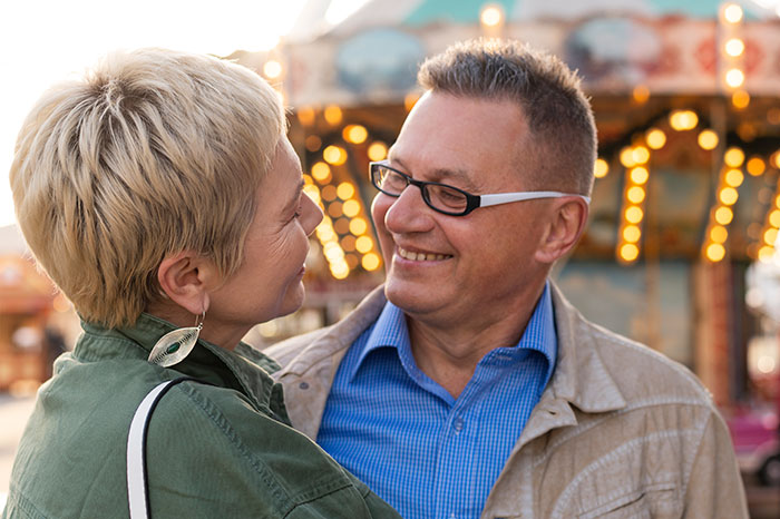 A smiling couple, possibly a Dad and Stepmom, looking at each other affectionately with amusement park lights in the background.