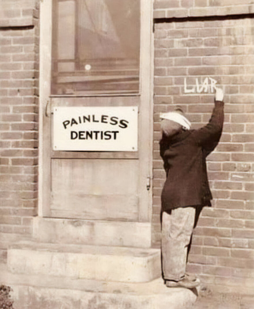 A child writes LIAR on a brick wall next to a Painless Dentist sign, a fascinating photo showing history.