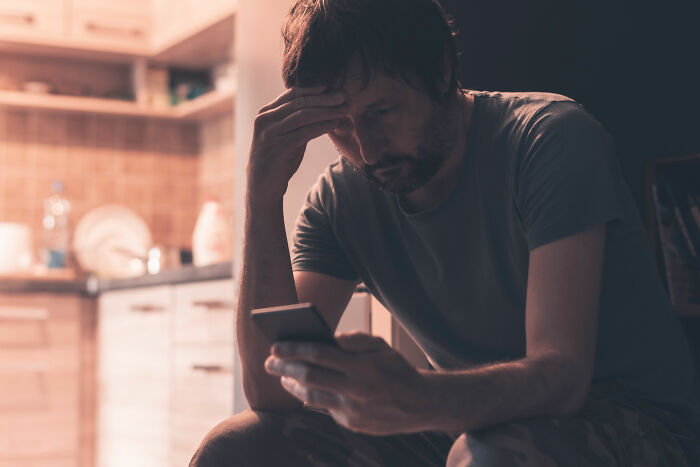 A distressed man looking at his phone in a kitchen, discovering he was being cheated on.
