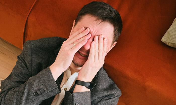 A man in a suit jacket covers his face, wincing. Patient stories can be intense; definitely not for the weak.