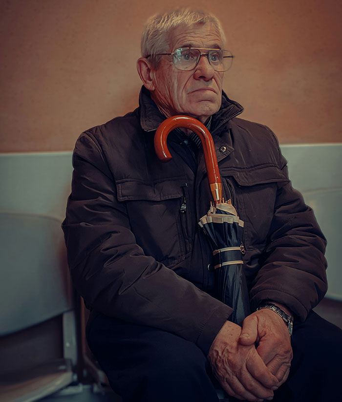 Elderly man with glasses and umbrella, deep in thought. Relates to Patient Stories and medical experiences.